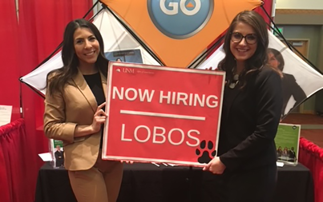 2 business women at a job fair holding a sign saying 'now hiring lobos'